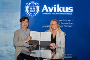 Dark haired man and blonde lady stand with signed document informant of a branded panel