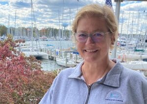 Headshot of smiling woman with picture of boats in marina in background.