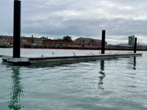 Floating breakwater attached to piles with military buildings in the background