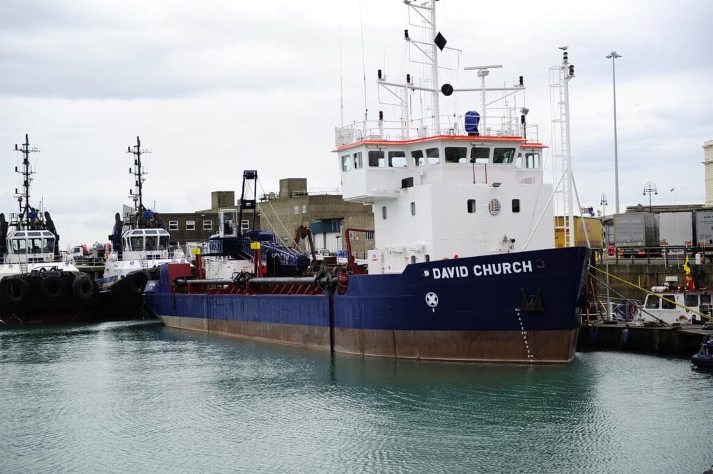 a large blue dredging vessel moored along side a pontoon in a port