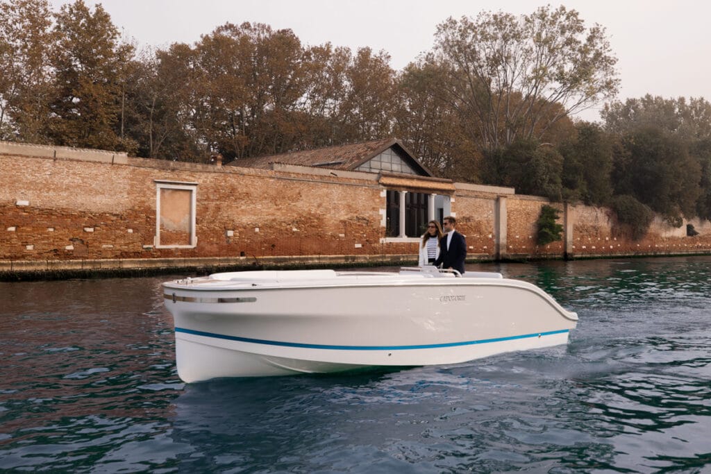 Electric boat afloat in front of a red brick wall with two people onboard