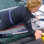 A woman lies on a paddleboard mid-rescue