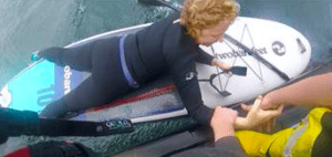 A woman lies on a paddleboard mid-rescue