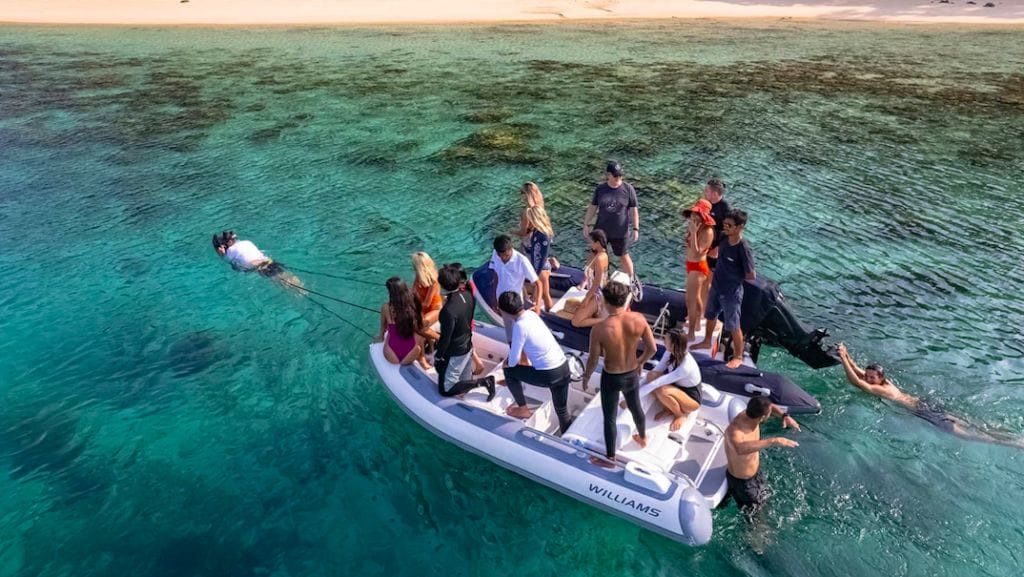 Hand held sea scooter pulls two boats full of people in clear sea