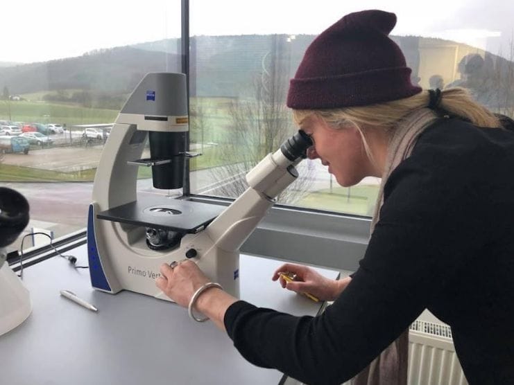 Scientist in hat peers down grey microscope