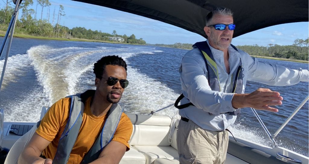 Two men on speedboat at helm, one man standing and pointing