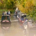 A canal boat meanders along a canal past several other boars moored to banks