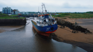 cargo ship stuck on sand as it grounds at Port of Silloth. Harbour entrance is enticingly close in background