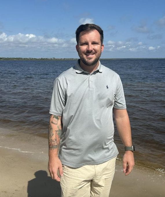 A man smiles at the camera - wearing a t-shirt on the beach. Jesse Carpenter joins Highfield Boats as it takes on four new dealers