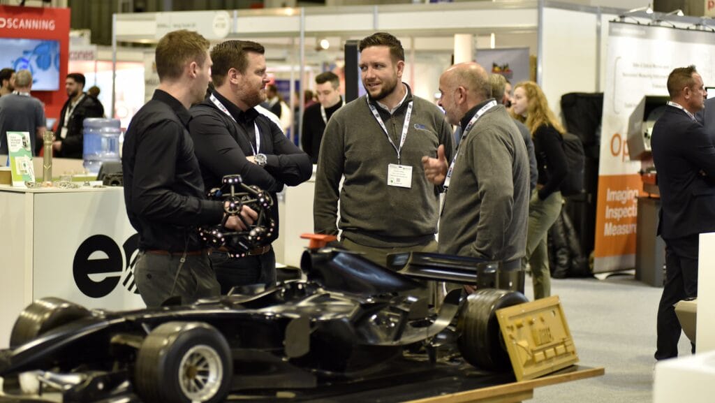 four men stand around a car discussing battery collaborations between the marine and automotive industries