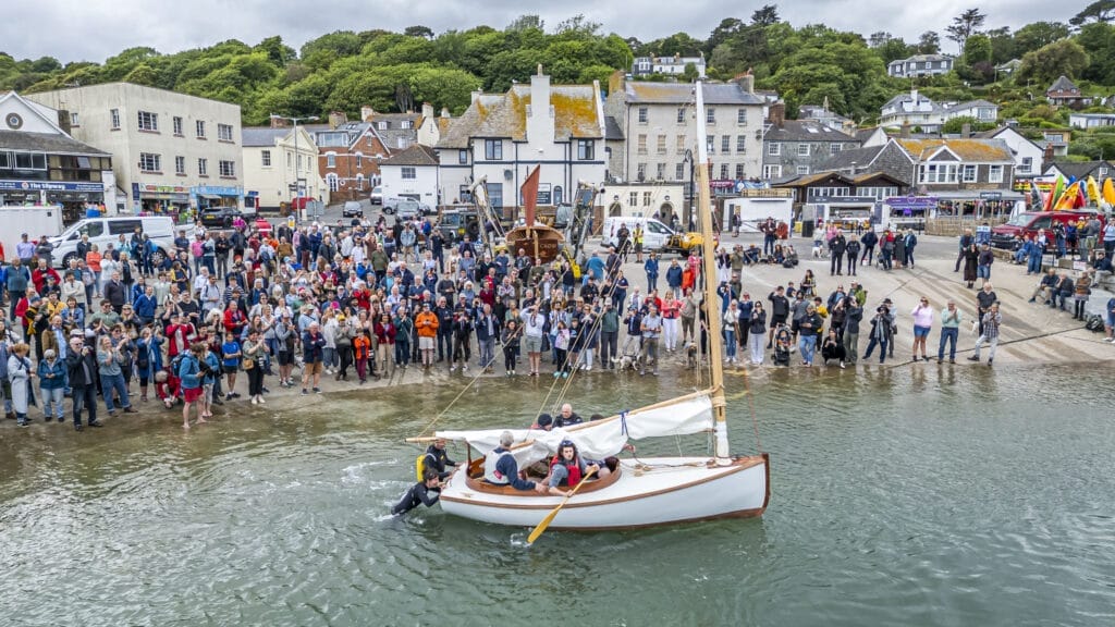 traditional small launch boat in harbour with a small crowd on harbour front