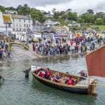 crowd on harbour bank and small traditional wooden launch in foreground