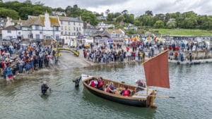 crowd on harbour bank and small traditional wooden launch in foreground