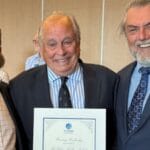 Three men in suits with a certificate