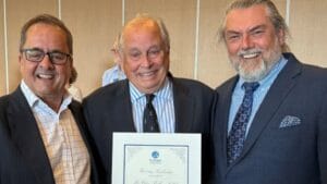 Three men in suits with a certificate