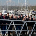 group of people in winter jackets standing on gangway with marina in background