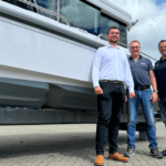 Three men stand in front of a boat