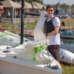 Four sailors stand around dinghy laughing