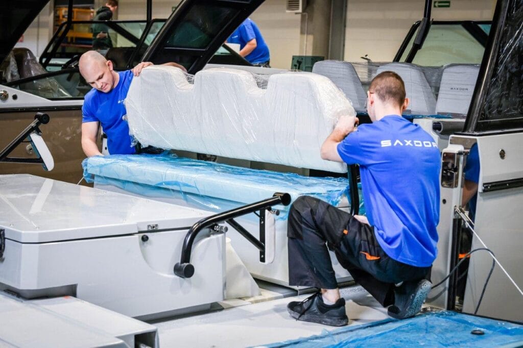 two factory works wearing blue t shirts pulling sofa seat back into place on motor boat cockpit in factory