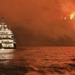 night shot with raging fire on hillside and yacht on the water in foreground