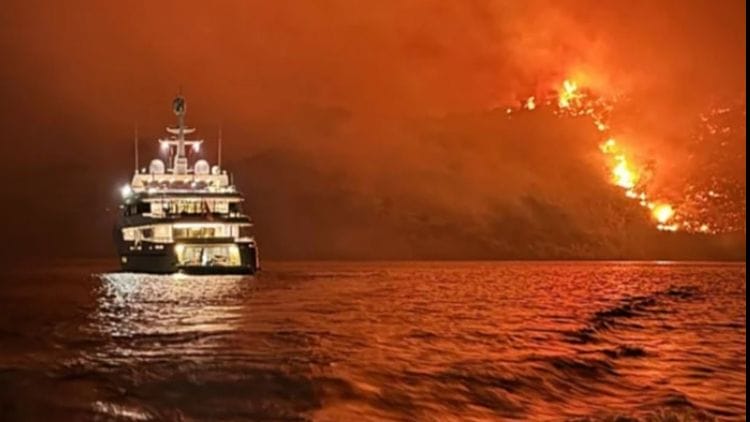 night shot with raging fire on hillside and yacht on the water in foreground