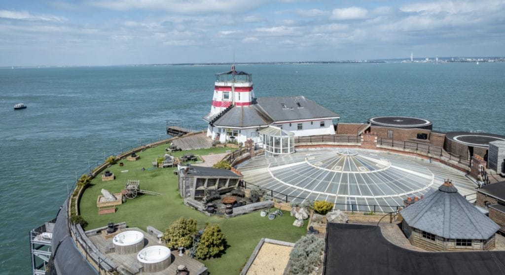 renovated granite fort off coast with striped lighthouse and sun terrace