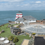 renovated granite fort off coast with striped lighthouse and sun terrace