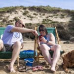 Two people sit in deckchairs on the beach using a mobile phone.