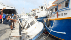 Fishermen try to move boats which have been crushed against dock in Hurricane Beryl
