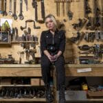 A woman sits in a workshop surrounded by tools.