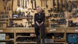 A woman sits in a workshop surrounded by tools.