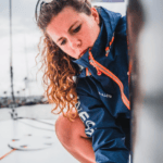 Sailor dressed in blue and orange INEOS jacket works on boat