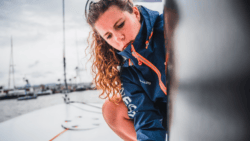 Sailor dressed in blue and orange INEOS jacket works on boat