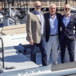 Three men stand on a boat, They're from Evoy and Vita and are now working together