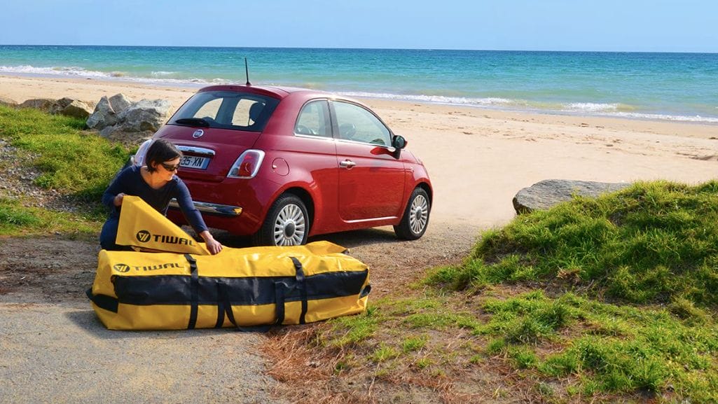 Sailor on beach packs Tiwal inflatable sailboat / dinghy into small red car