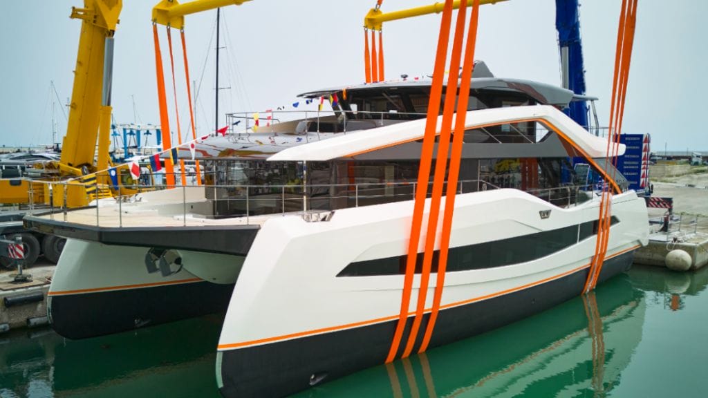 side view of Wider Yachts launch Fano Italy WiderCat 92. BOat lowered into water in orange sling