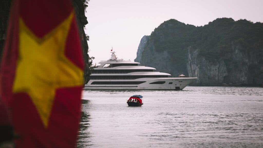 A superyacht sails through a bay in Vietnam with the Vietnam flag in foreground.