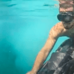 Man dragged along underwater by sea scooter. He wears a dive mask