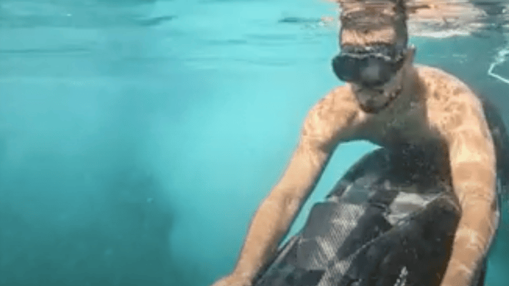 Man dragged along underwater by sea scooter. He wears a dive mask