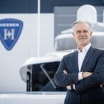 man in suit with Heesen emblem and superyacht bow behind