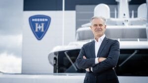 man in suit with Heesen emblem and superyacht bow behind