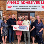 A gorup of people holding a banner stand under another banner. The first is Polymarine, the second is Anglo Adhesives.