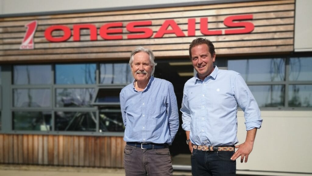 Two men in front of a OneSails sign
