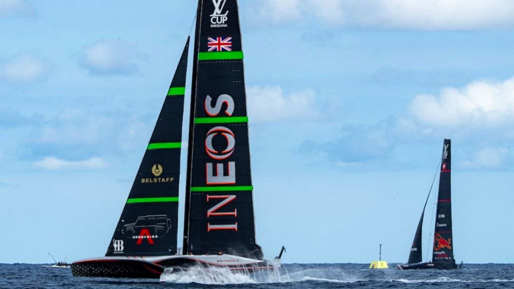 RIta - INEOS Britannia's America's Cup boat sails across foreground with luminous green trim on black sails