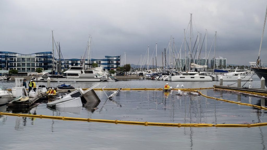 semi submerged yacht on its side with environmental yellow boom around area to stop oil spill