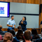 two people talk in a lecture theatre in front of a crowd