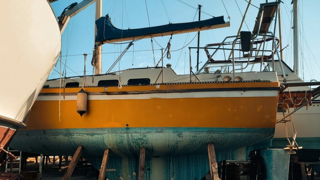 A yellow and white boat sitting on top of a beach in dry dock.