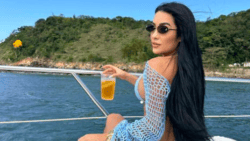 Lady with back to camera raises drink while sat onboard a boat.