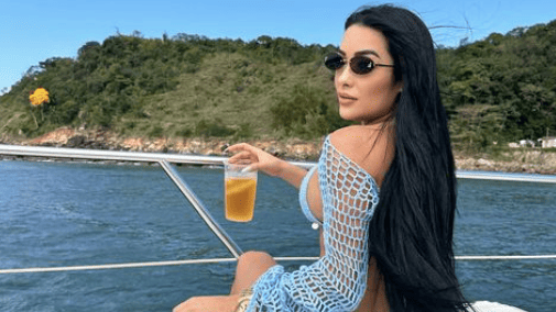 Lady with back to camera raises drink while sat onboard a boat.