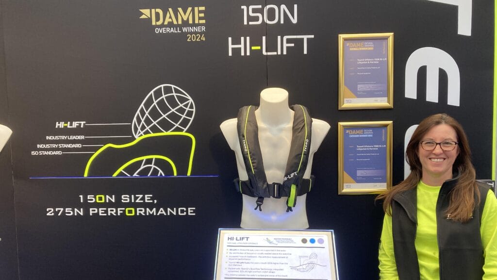 Hermione Barfield from TeamO stands in a booth displaying award winning Hi-Lift Lifejacket. She wears yellow with a black gilet